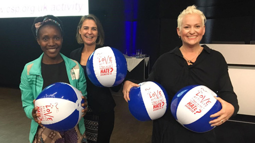 Three women stand holding blue and white beach balls