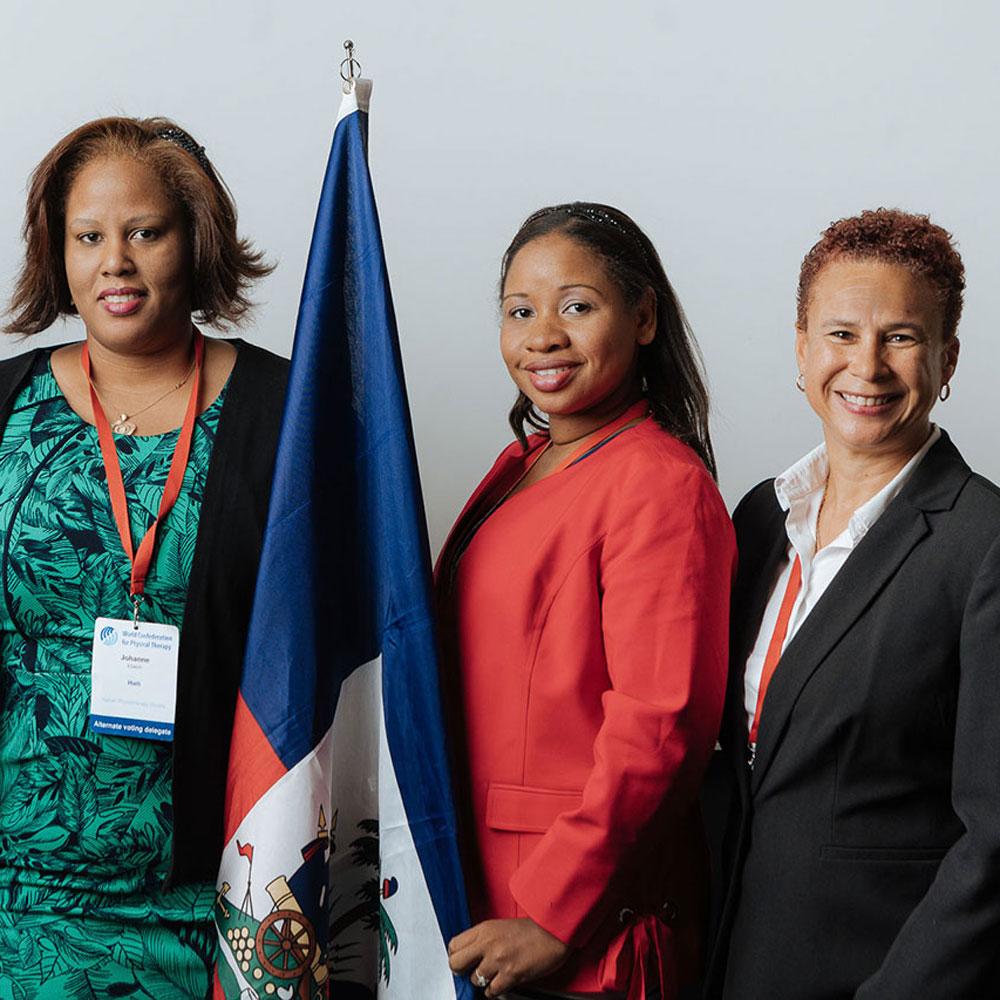 Three women standing together, one holds the Haitian flag