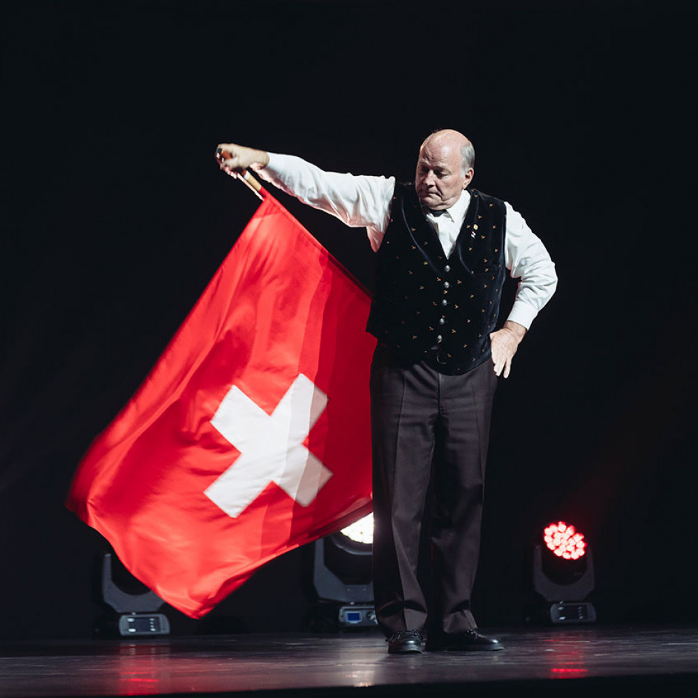 Seorang pria di atas panggung memegang bendera Swiss yang besar