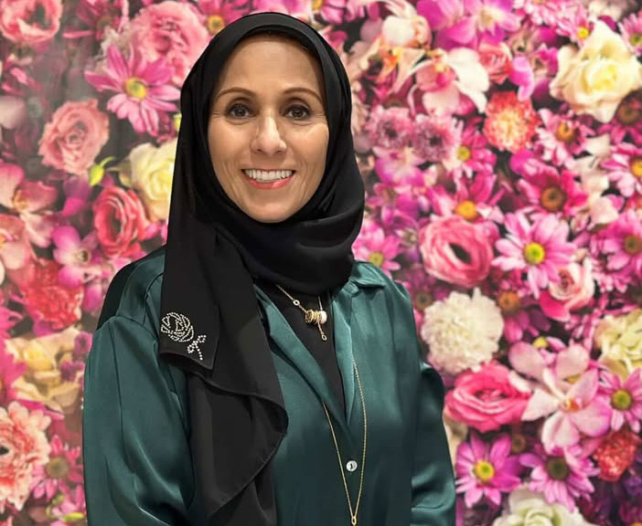 A head and shoulders photograph of a woman smiling at the camera in front of a flowered background