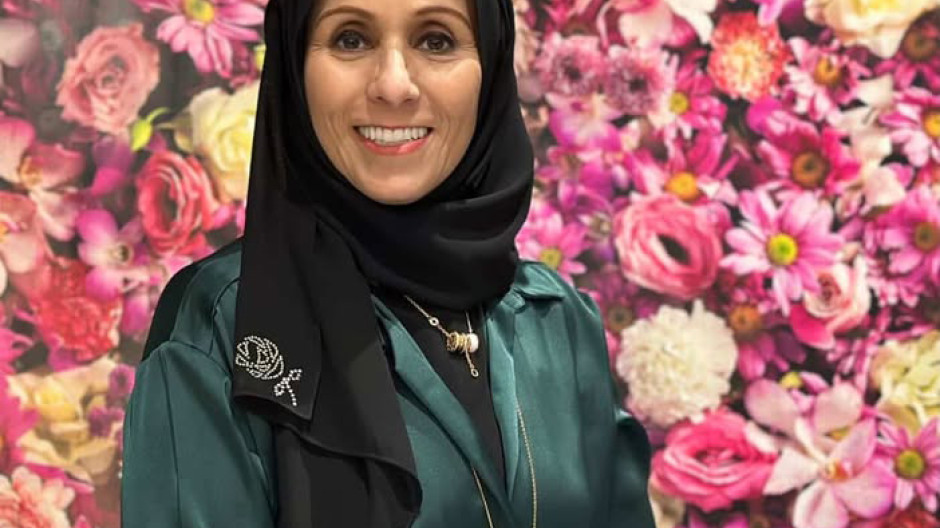 A head and shoulders photograph of a woman smiling at the camera in front of a flowered background