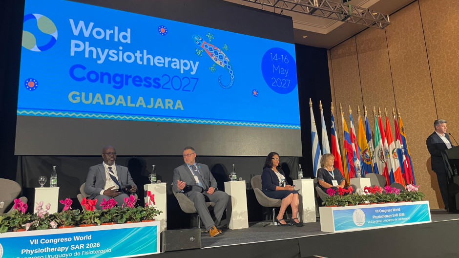 A group of panellists on stage discussing in front of a number of South American flags. The screen reads World Physiotherapy Guadalahara 2027