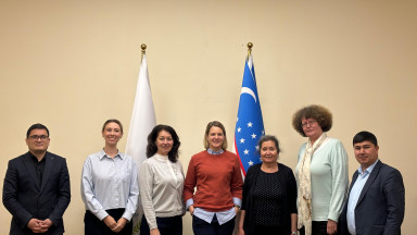 Seven individuals standing in a row in front of two flags, one of which is the flag of Uzbekistan